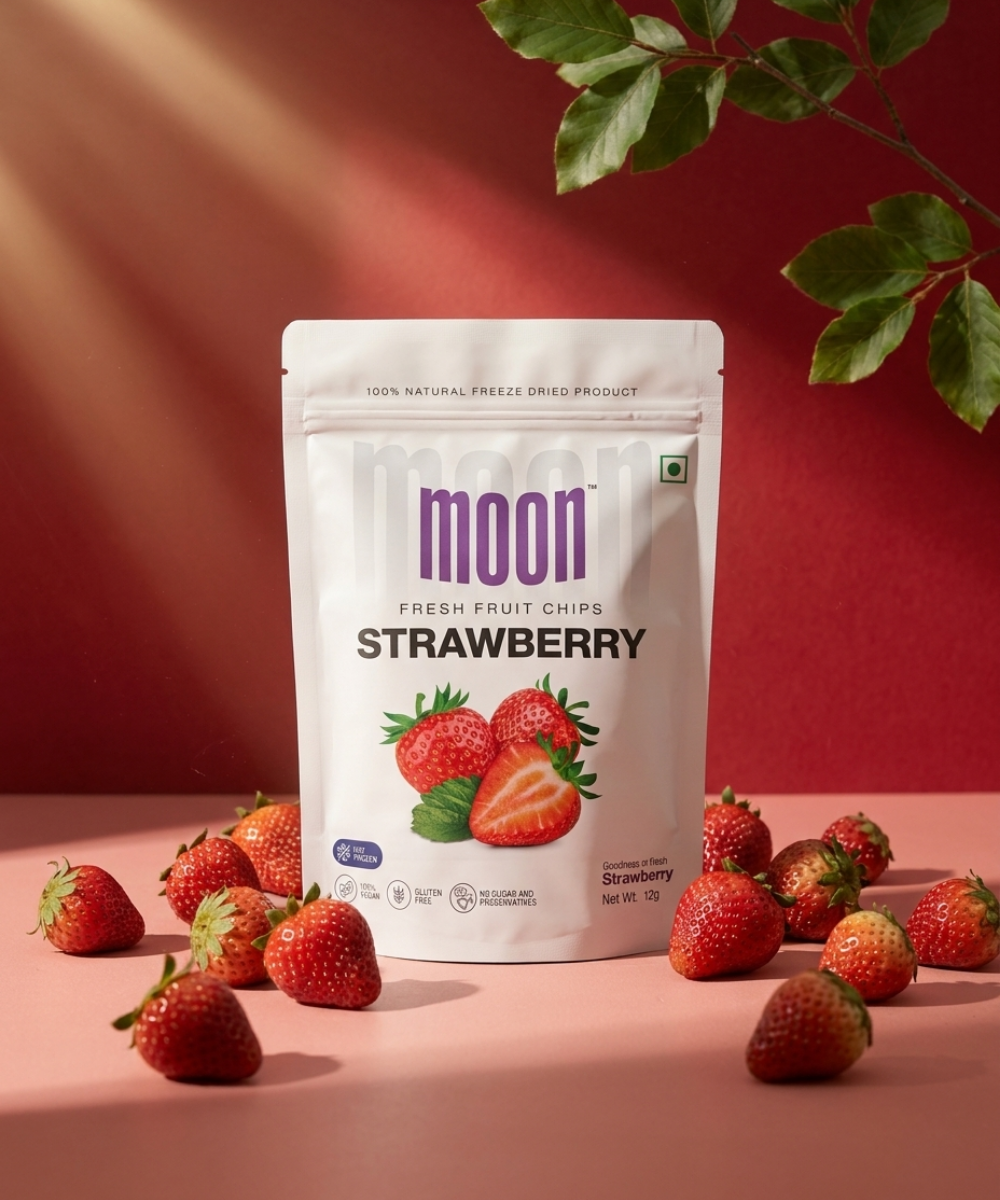 Themoonstoreindia's Moon Freeze Dried Strawberry is shown upright on a pink surface, surrounded by whole and sliced strawberries with green leaves in the background.