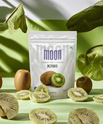 A white resealable pouch of Themoonstoreindia's Moon Freeze Dried Kiwi, high in vitamin C and fiber, is displayed with whole and sliced kiwis, freeze-dried kiwi chips, and green leaves on a light green surface.